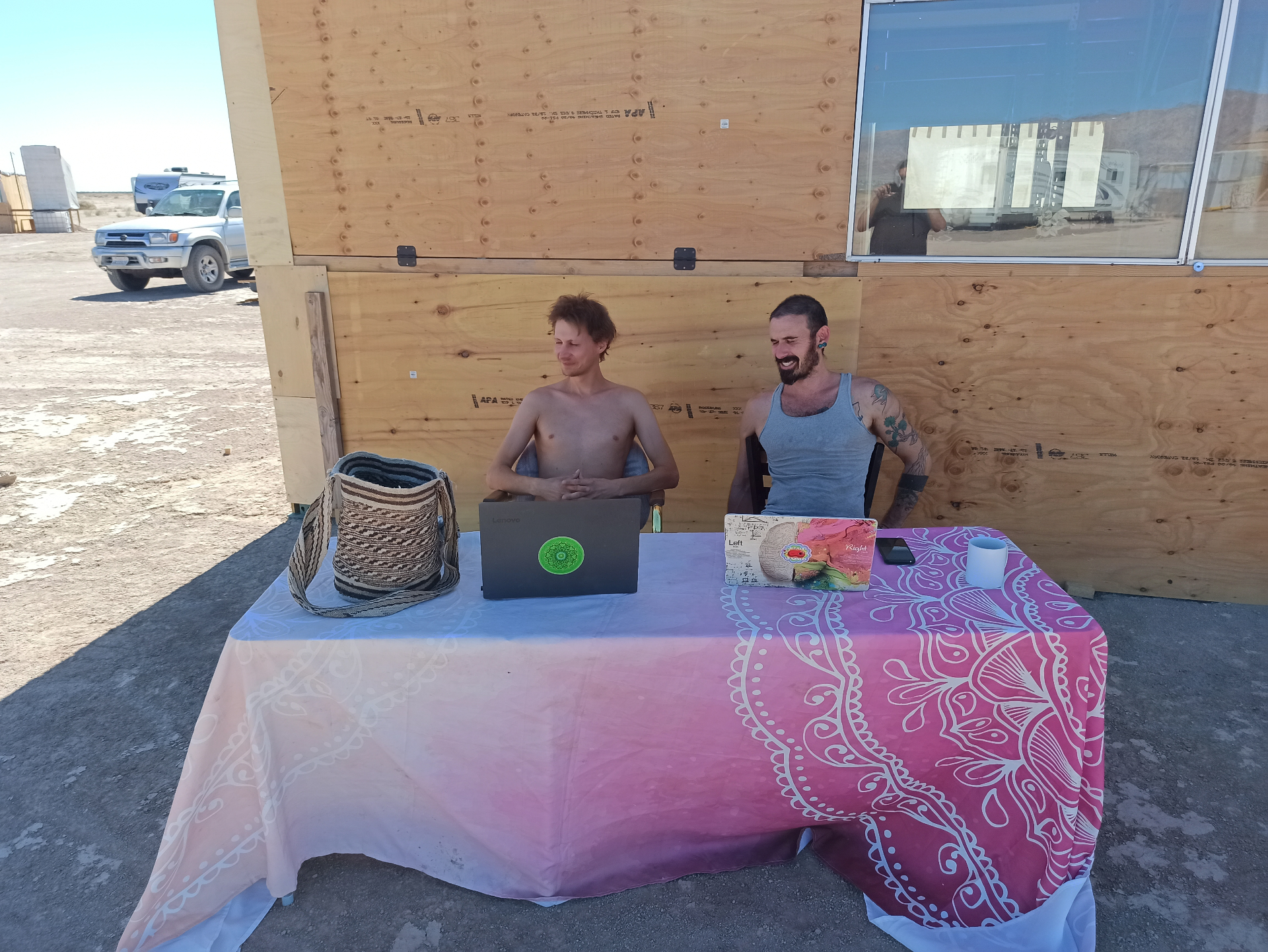 Two campmates working at a laptop station outside the build