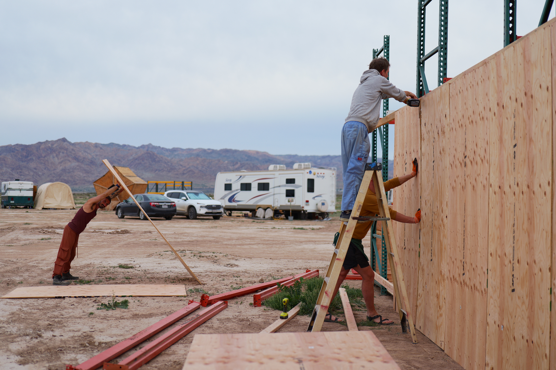 Campmates raising a plywood wall against the mountains