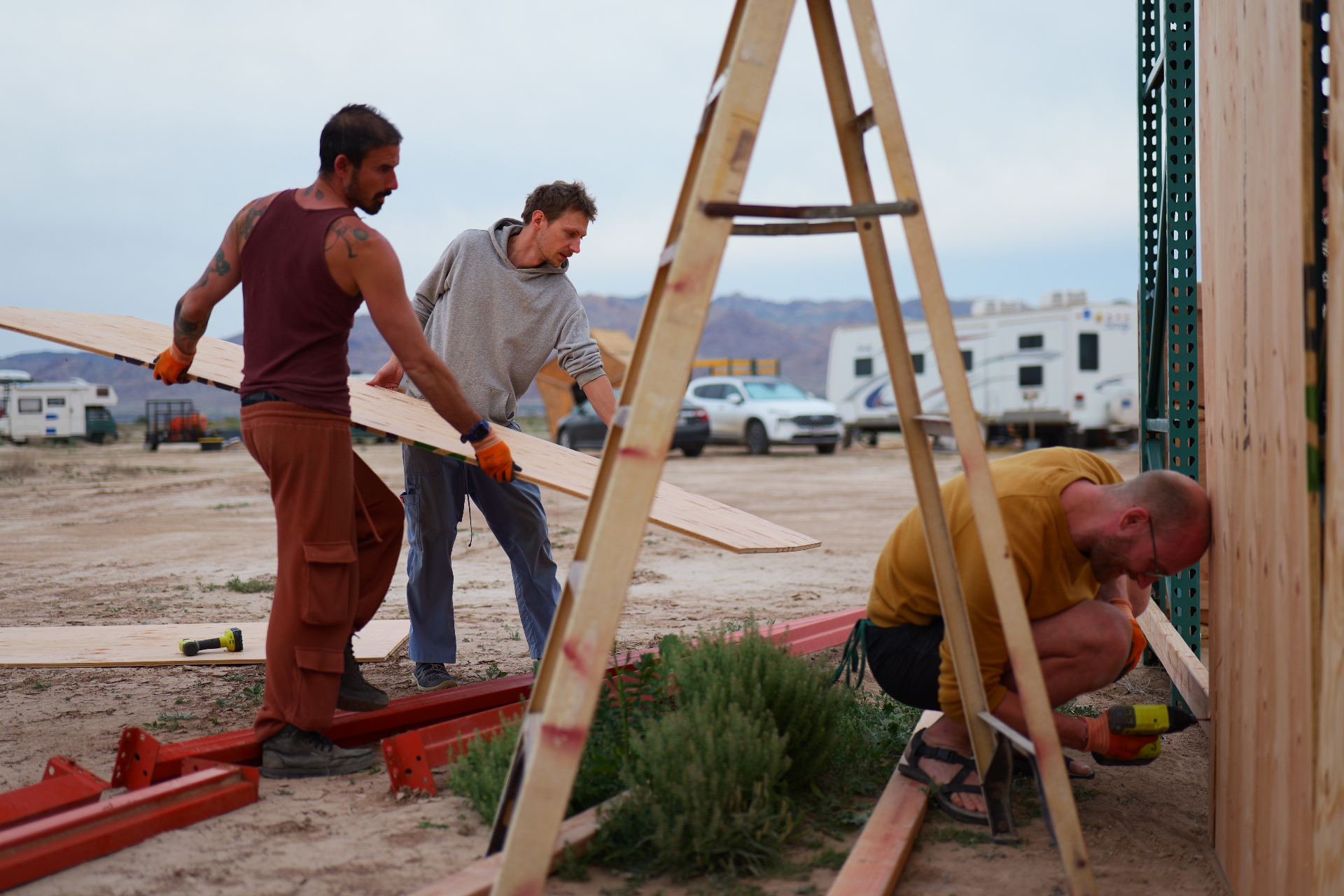 Three builders carrying lumber during camp construction